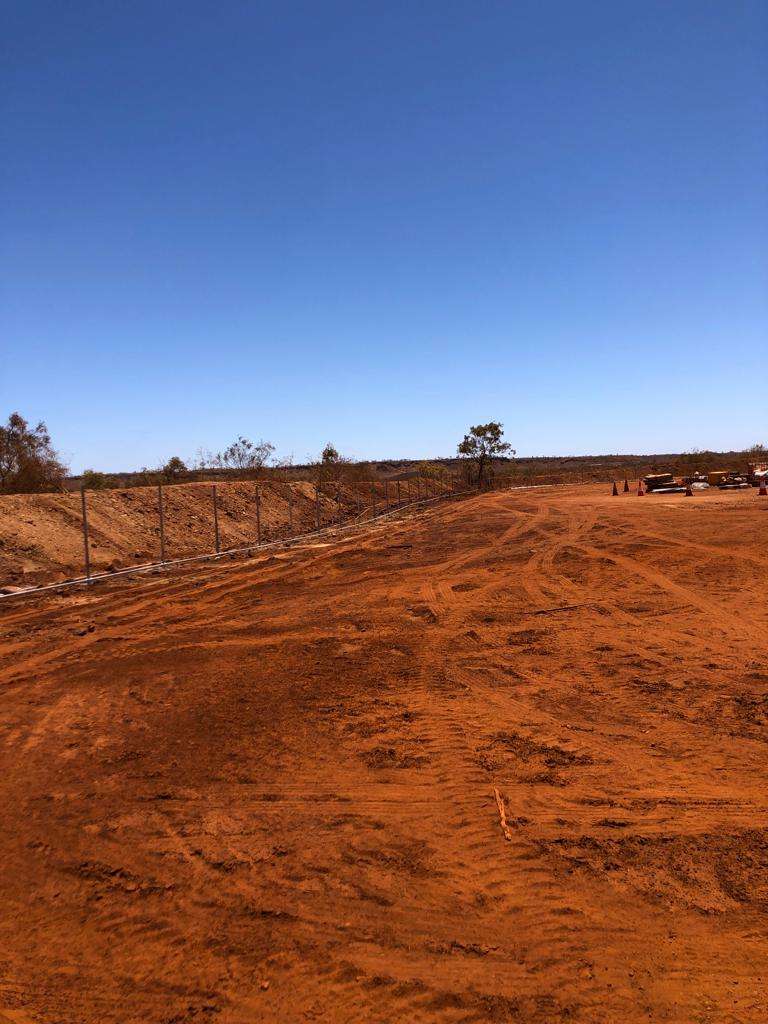 Long chain link fence run across a cleared red-dirt site
