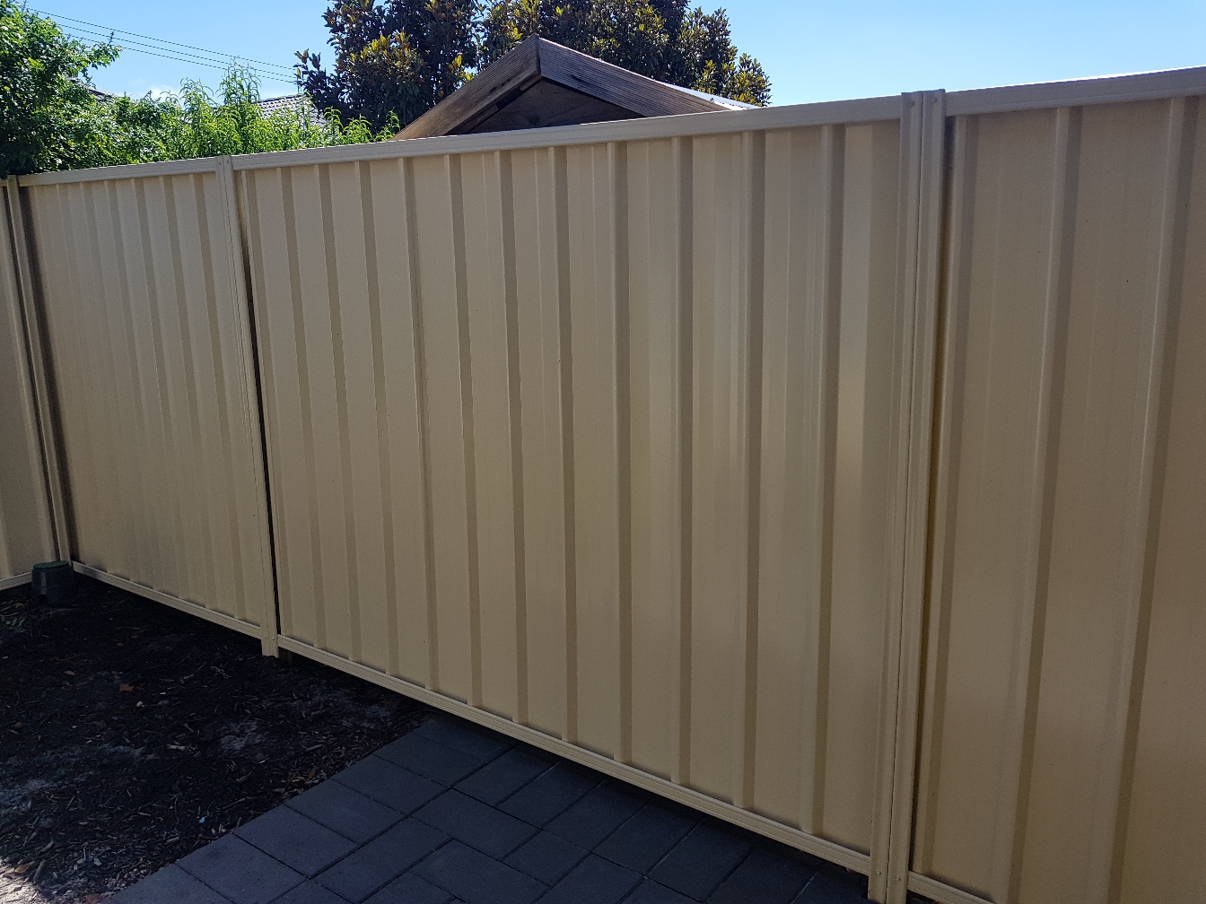 Cream Colorbond boundary fence beside paving