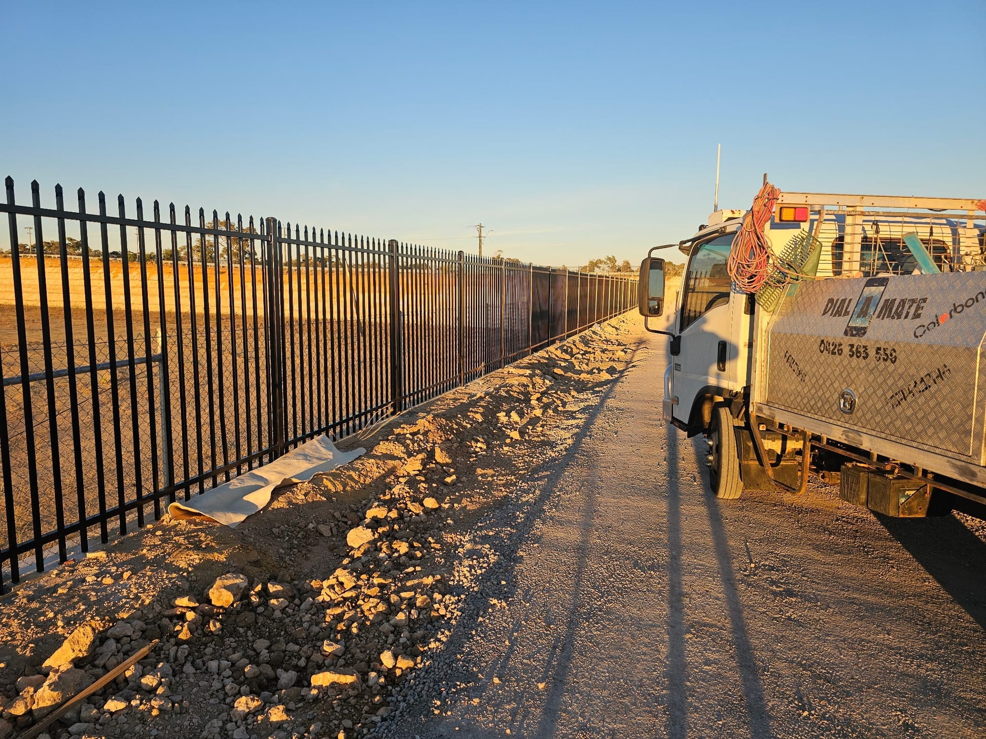 Long black garrison security fence run at golden hour with the Dial-A-Mate truck parked alongside