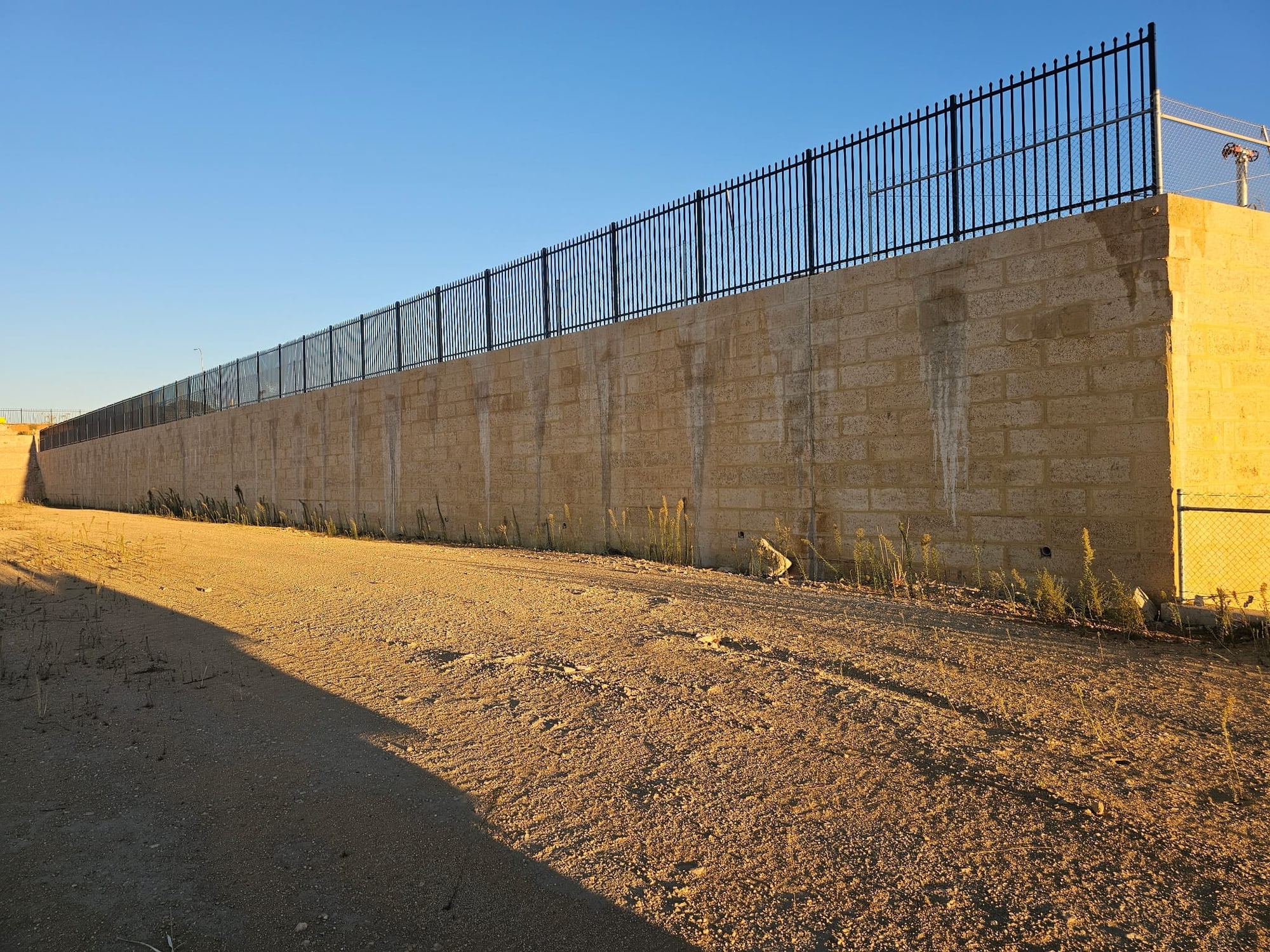 Black garrison security fence topping a limestone block retaining wall