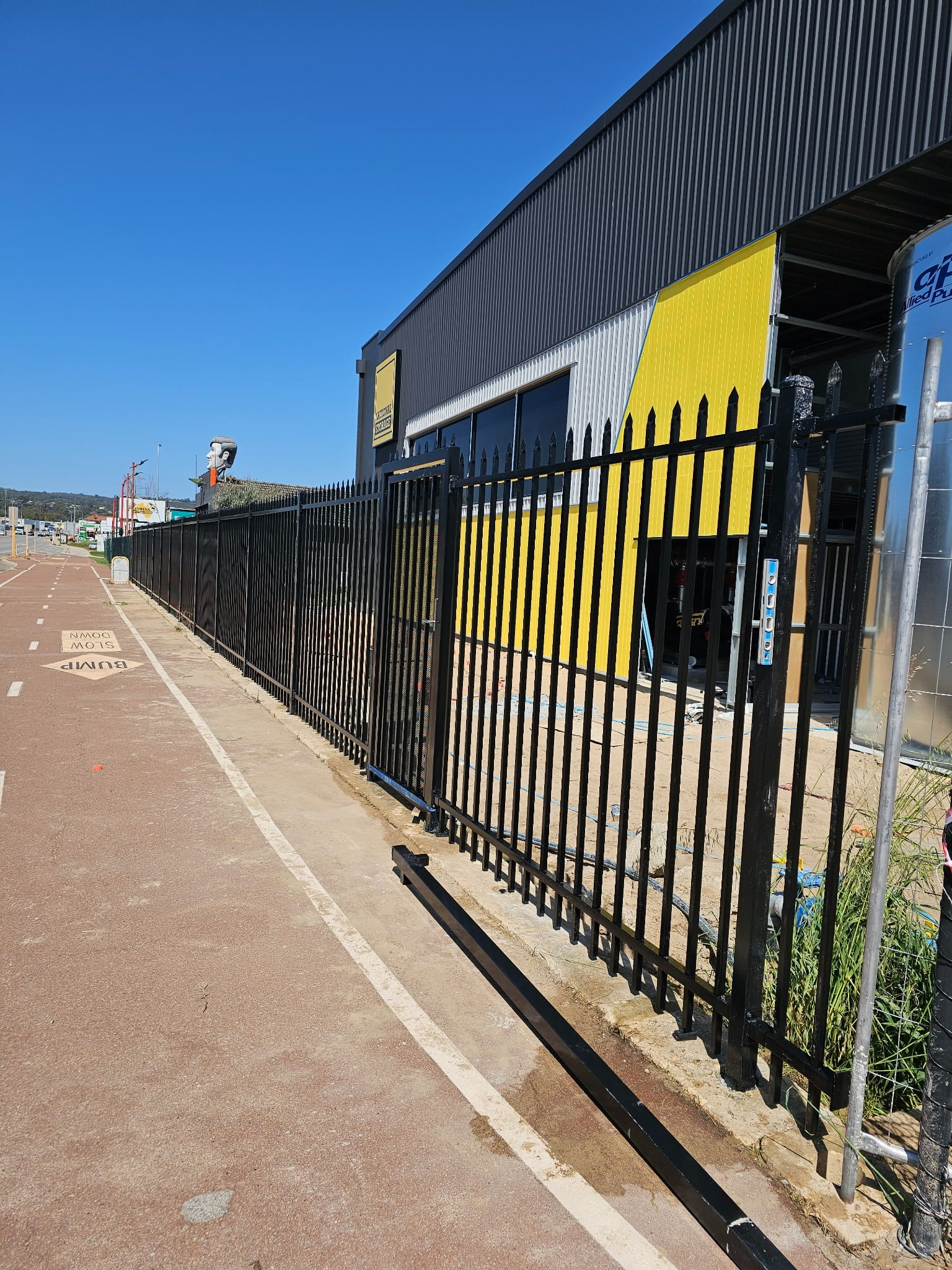 Black spear-top garrison fence and sliding vehicle gate at a commercial site