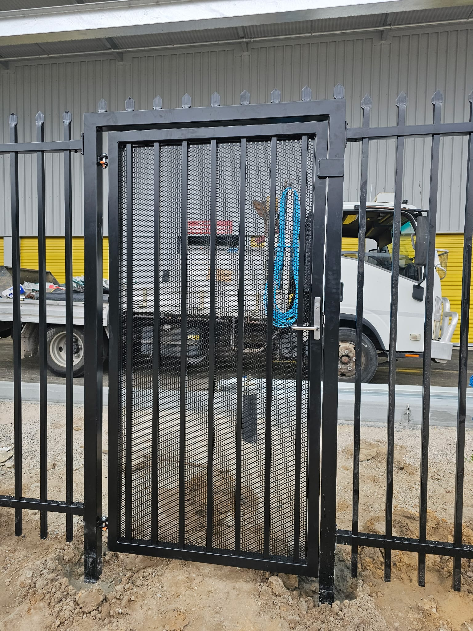 Garrison fence with a perforated mesh-infill pedestrian gate