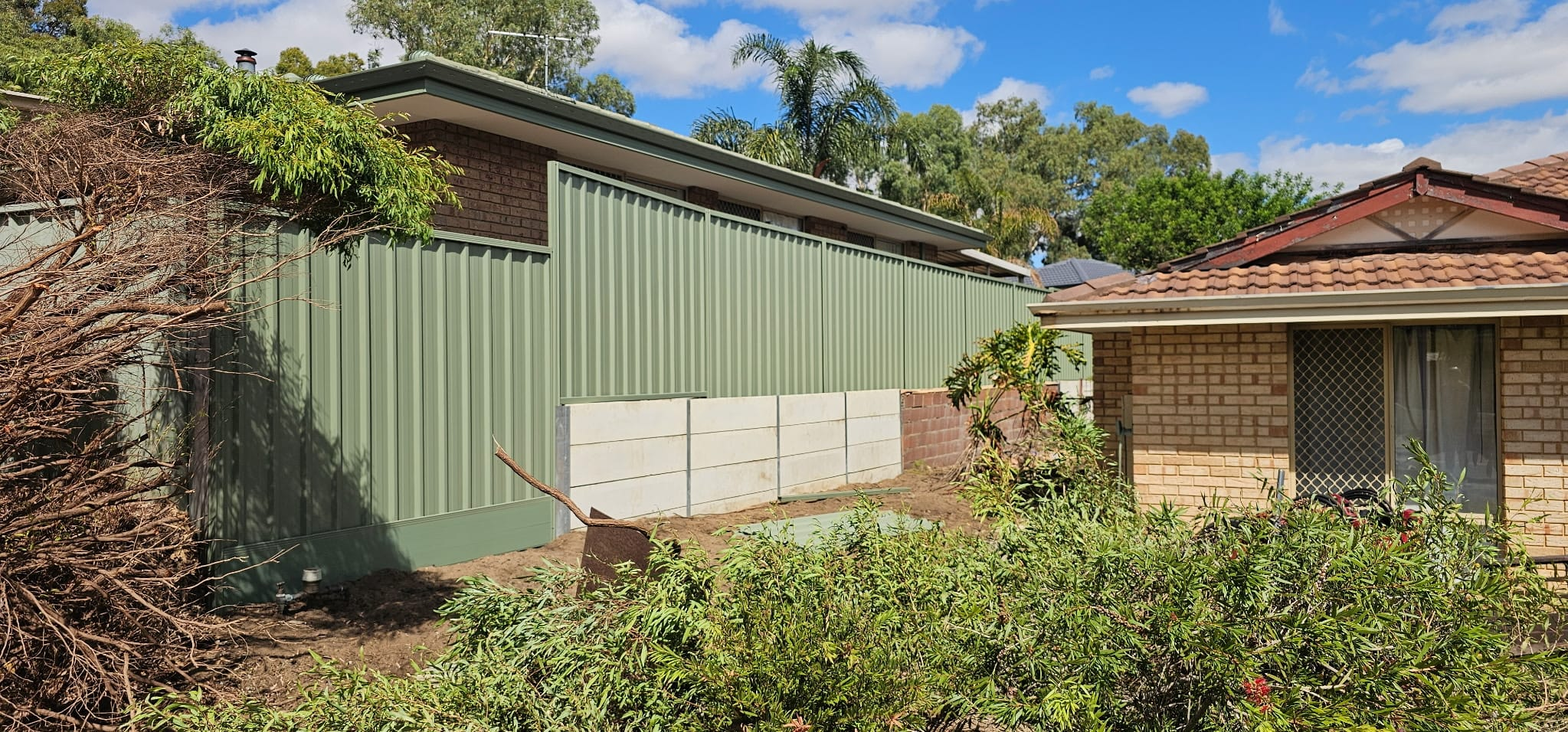 Pale green Colorbond fence above a concrete sleeper retaining wall