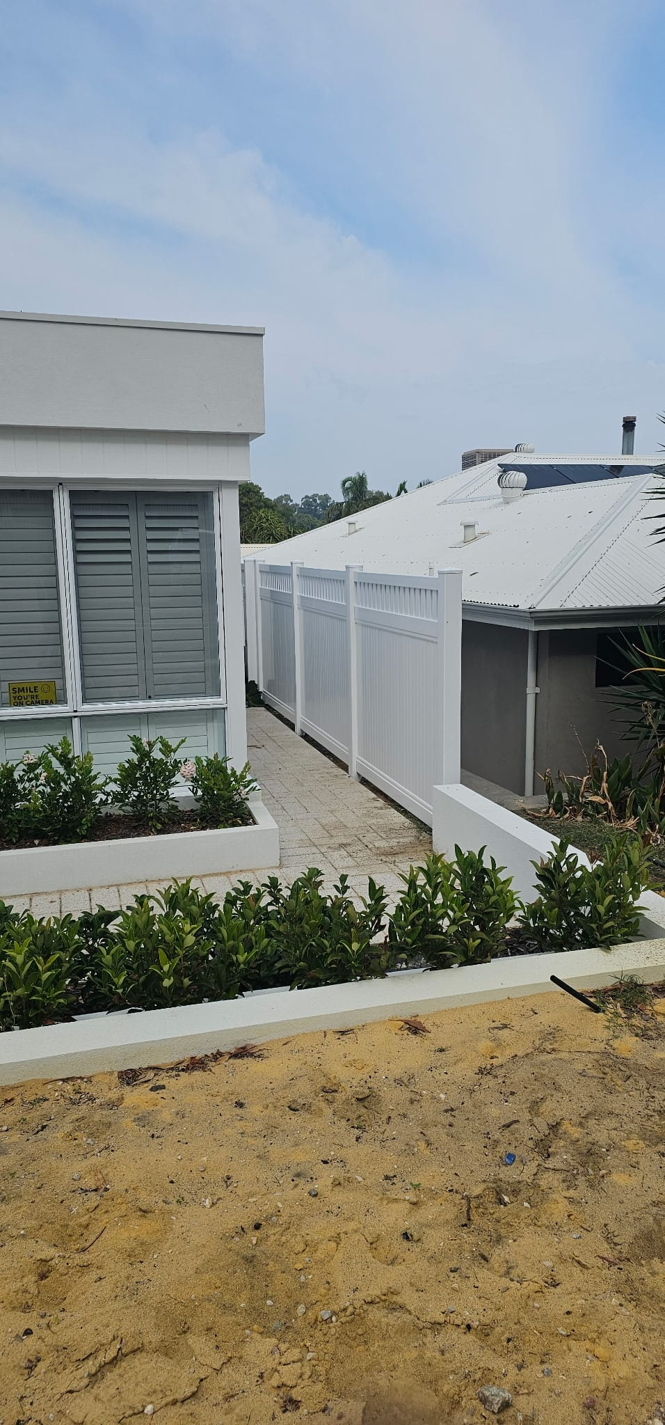 White privacy fence between two modern homes with rendered planters and clipped hedging