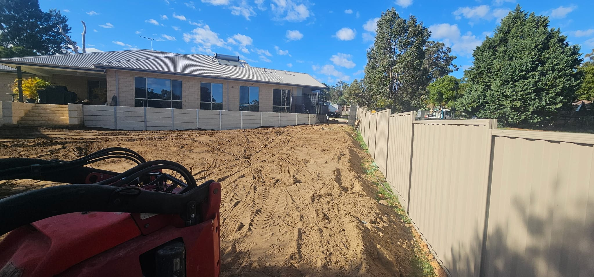 Bobcat earthworks beside a new sleeper retaining wall and Colorbond fence