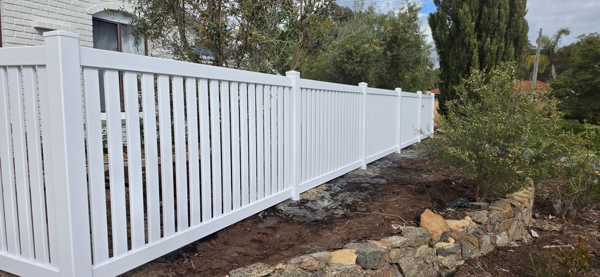 White PVC semi-privacy picket fence running along a residential boundary beside a white brick home in Perth