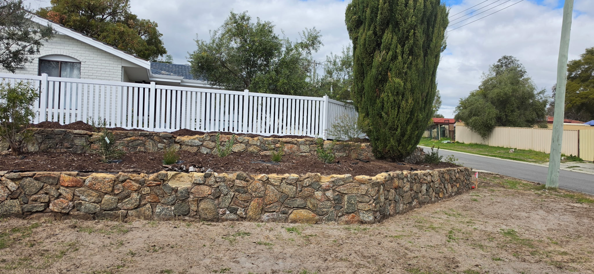 White PVC picket fence installed on top of a granite stone retaining wall at a street frontage