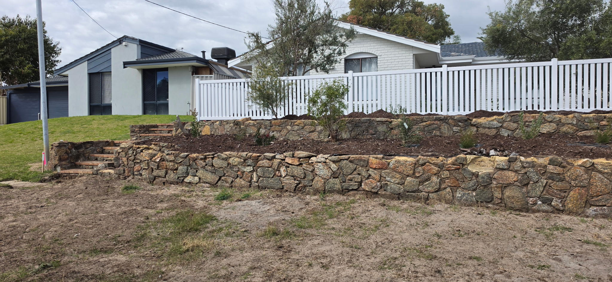 White PVC picket fence above tiered granite retaining walls with garden steps